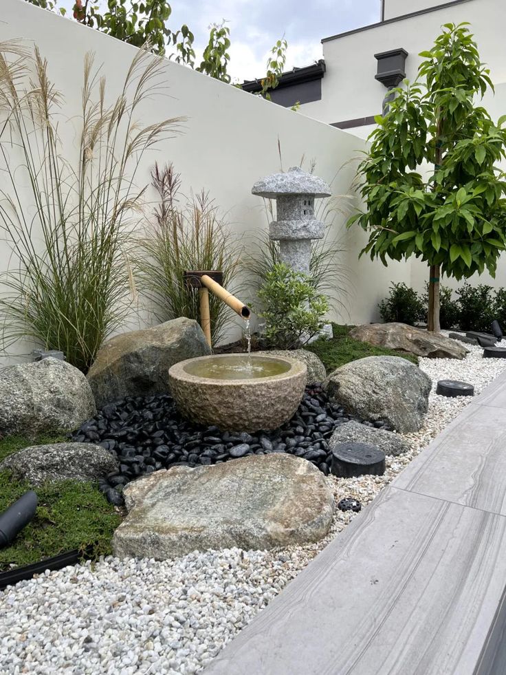 an outdoor garden with rocks, plants and water feature in the center is a fountain