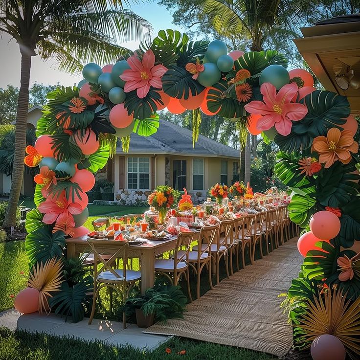 an outdoor table set up for a party with balloons and flowers on the top, surrounded by palm trees