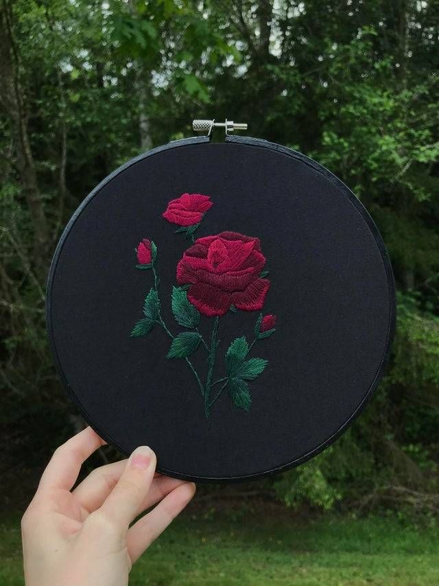 a person holding up a black embroideryed rose in front of some trees and grass