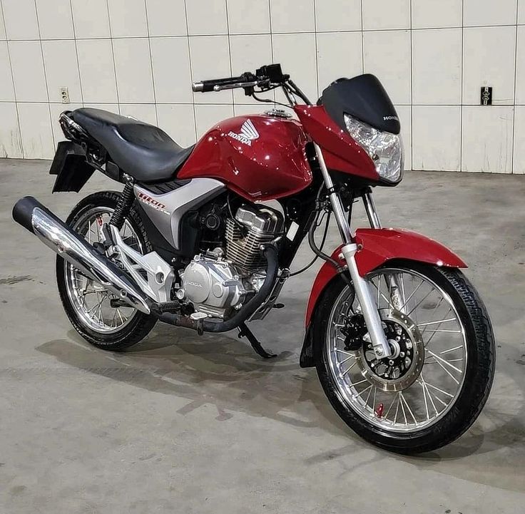 a red motorcycle parked in a garage next to a white brick wall and cement floor