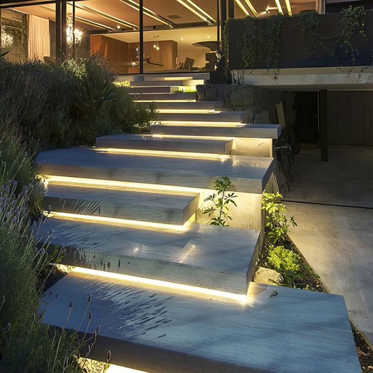 some steps that have been lit up with lights and plants in front of a house