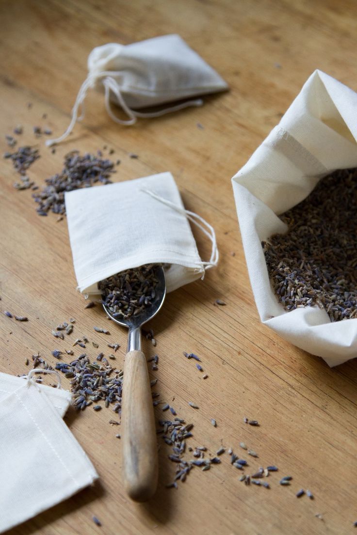 a wooden table topped with two bags filled with seeds next to a scoop of tea