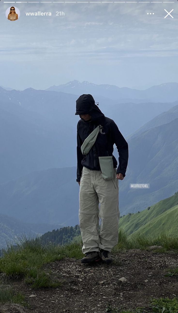 a man standing on top of a lush green hillside with mountains in the back ground