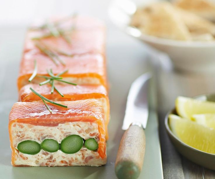 two slices of salmon with cucumbers and herbs on them next to a bowl of lemon wedges