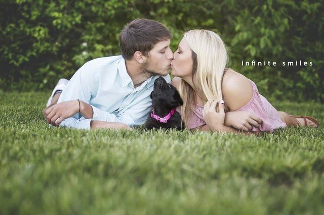 a man and woman laying in the grass with a dog on their lap, kissing