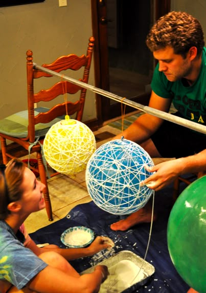 a man and two children are making balls out of yarn on a table with balloons