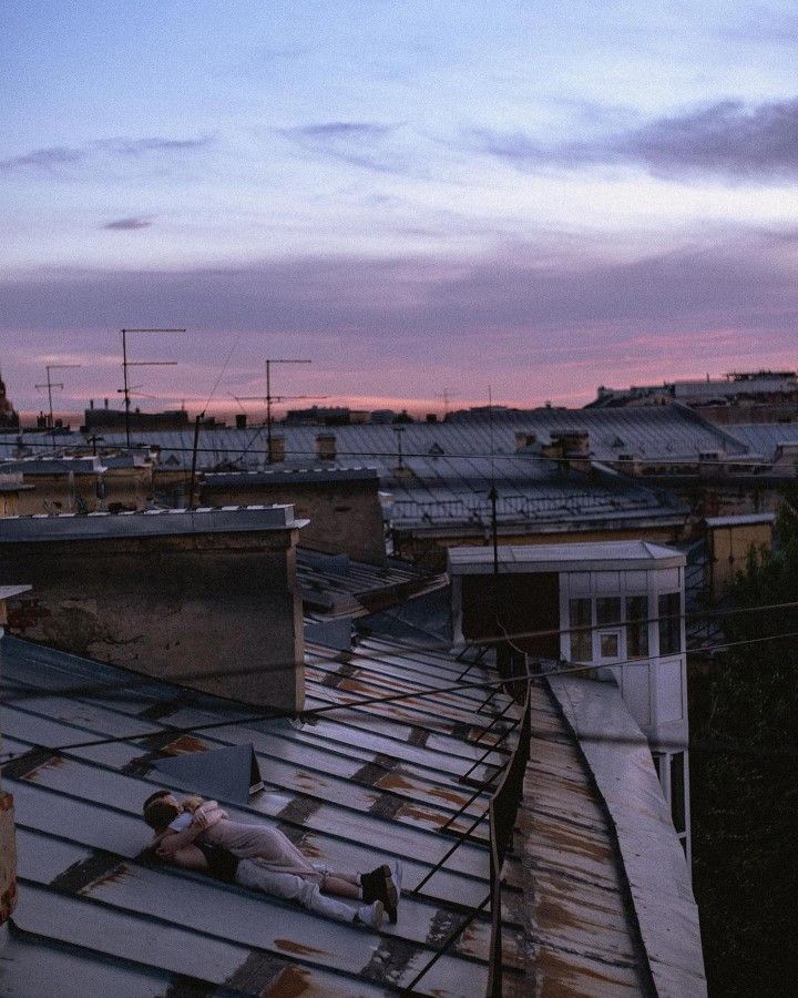 a man laying on top of a metal roof next to a tall building with lots of windows