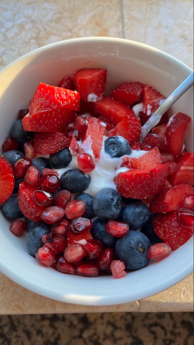 a bowl filled with strawberries, blueberries and pomegranate on top of a table