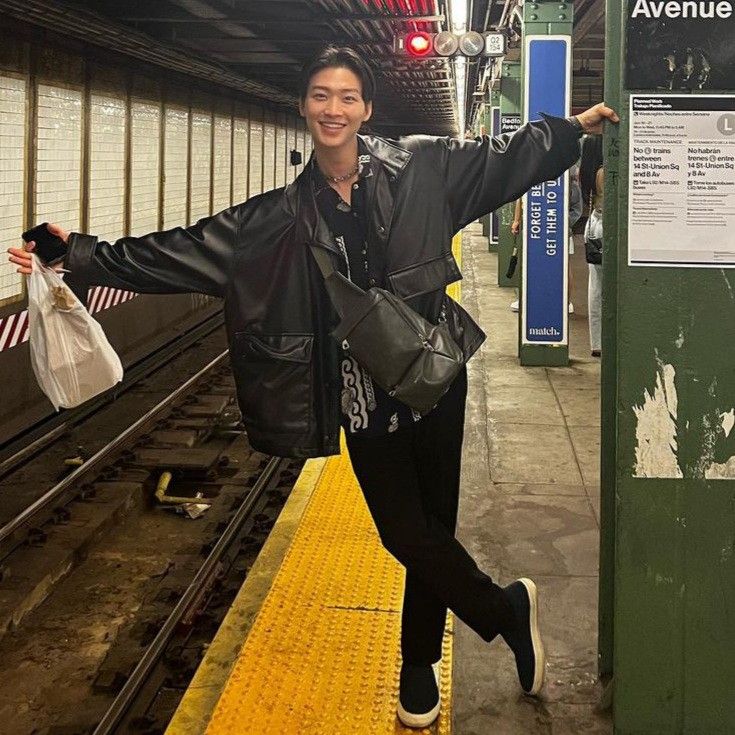 a woman in black jacket standing on train platform next to yellow and green rail way