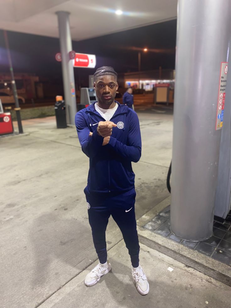 a man standing in front of a gas station with his arms crossed and looking at the camera