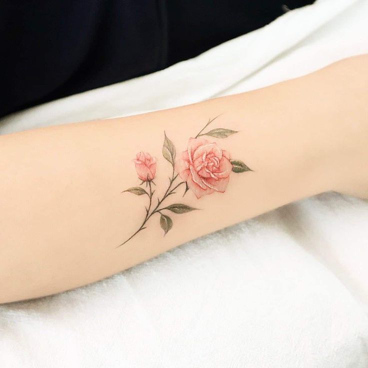 a woman's arm with pink roses on it and green leaves around the wrist