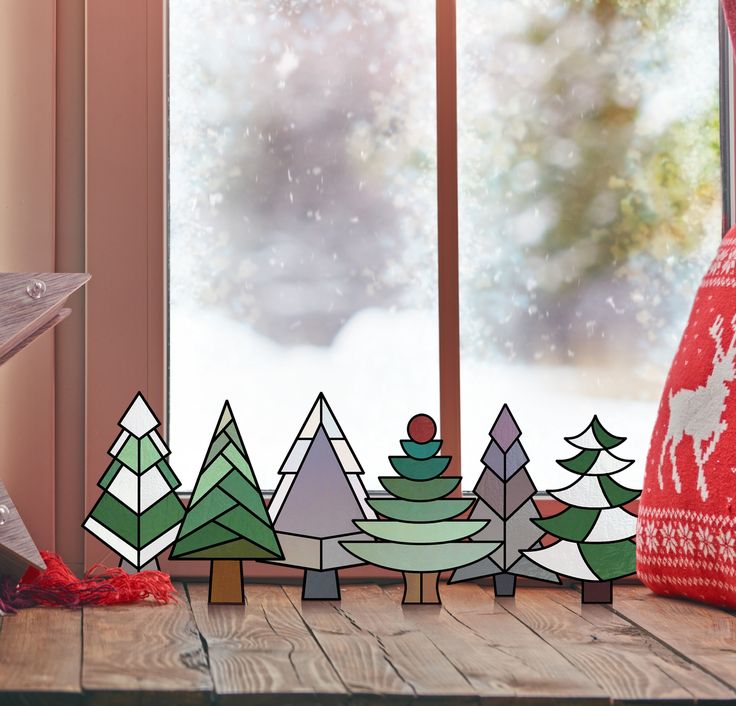 paper cut out christmas trees on a table next to a window with snow falling outside