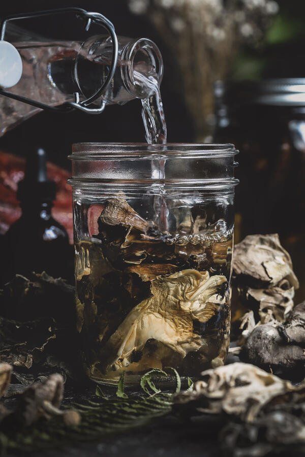 a glass jar filled with liquid pouring from a faucet over top of mushrooms