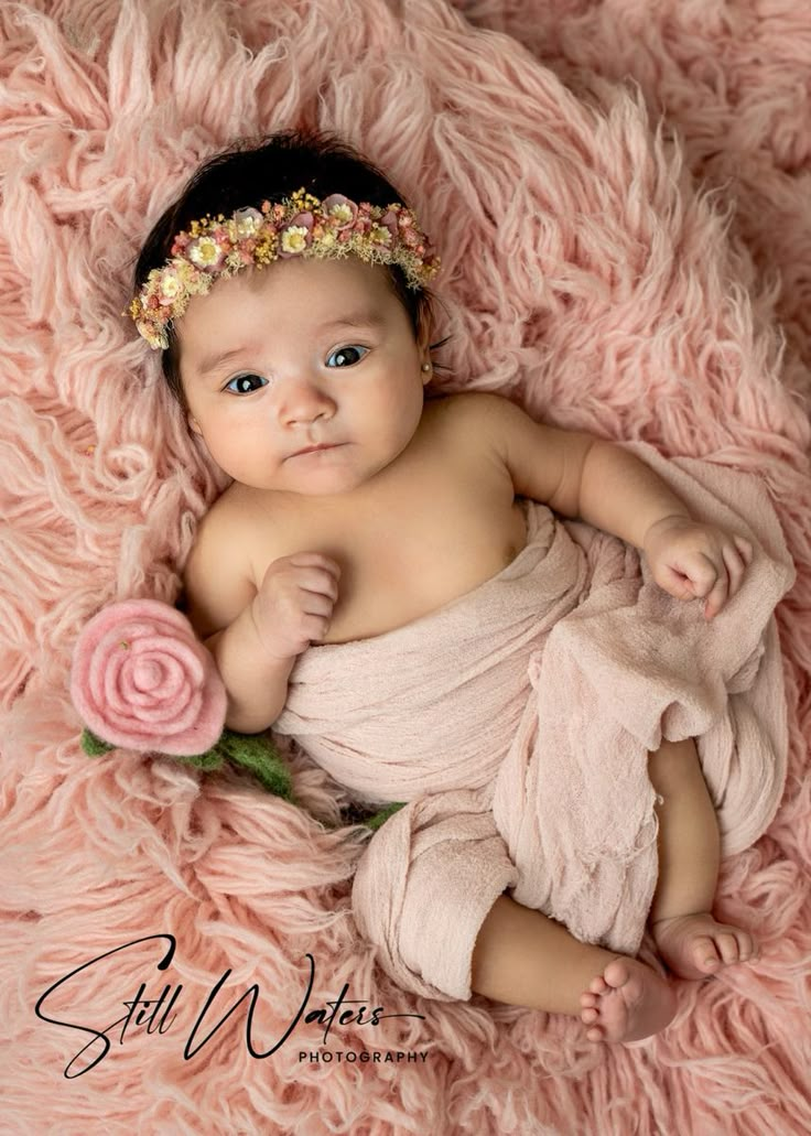 a baby is laying on a pink blanket with a flower in her hair