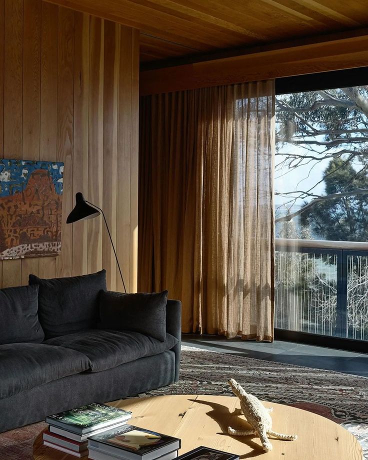 a living room filled with furniture and a large window covered in wood paneled walls