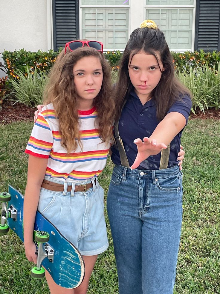 two girls standing next to each other in front of a house with their skateboards