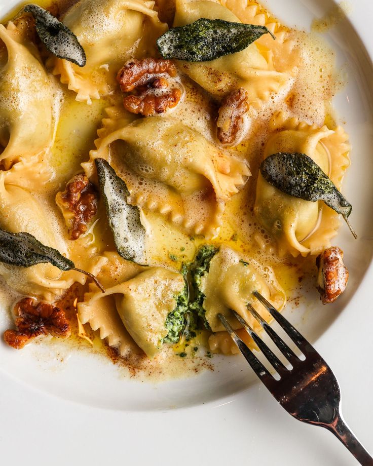 a white plate topped with pasta covered in sauce and spinach leaves next to a fork