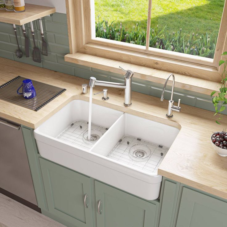 a kitchen sink with two faucets in front of a window and green cabinets