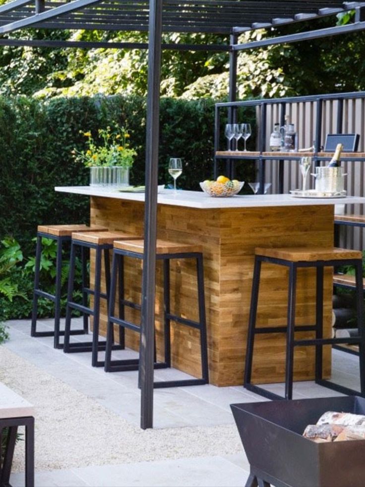 an outdoor bar with stools and tables under a pergolated roof, surrounded by greenery