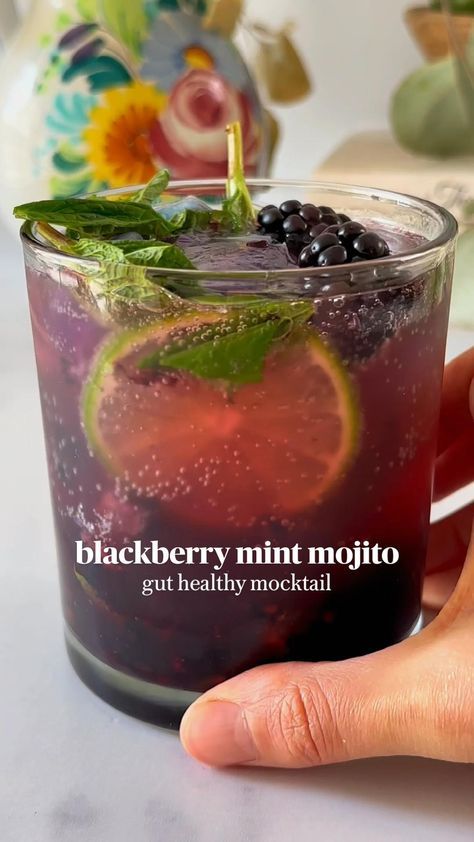 a hand is holding a glass filled with black berry mint mojito