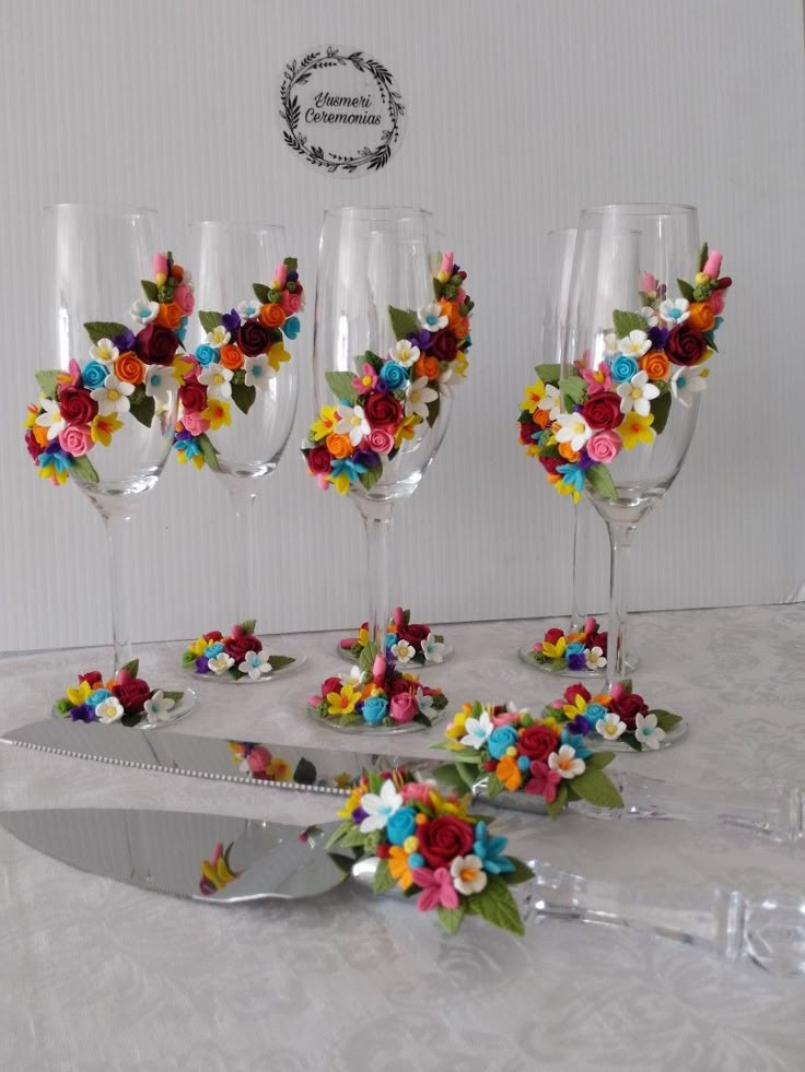 four wine glasses decorated with colorful flowers on a white table cloth and silverware knife