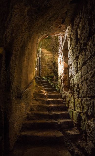 a stone tunnel with stairs leading up to the light at the end and dark lighting on the walls