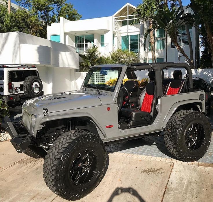 a gray jeep with red seats parked in front of a white building and palm trees