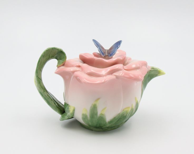 a ceramic teapot with a butterfly on it's top sitting in front of a white background