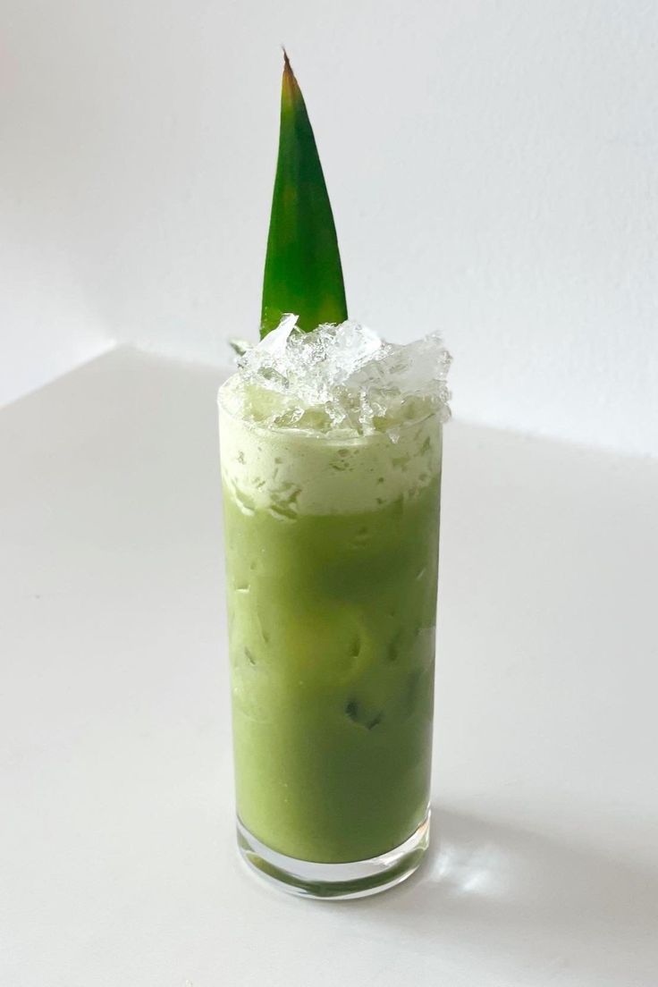 a green drink with ice in it sitting on a table next to a white wall