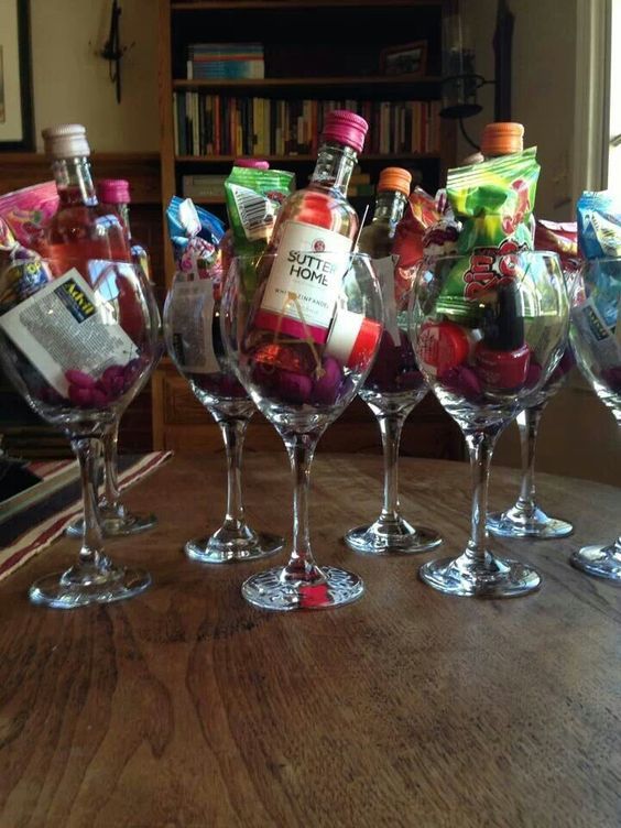 several wine glasses filled with different types of items on a table in front of a bookshelf