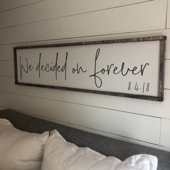 a wooden sign that says we decided on forever above a bed with white sheets and pillows