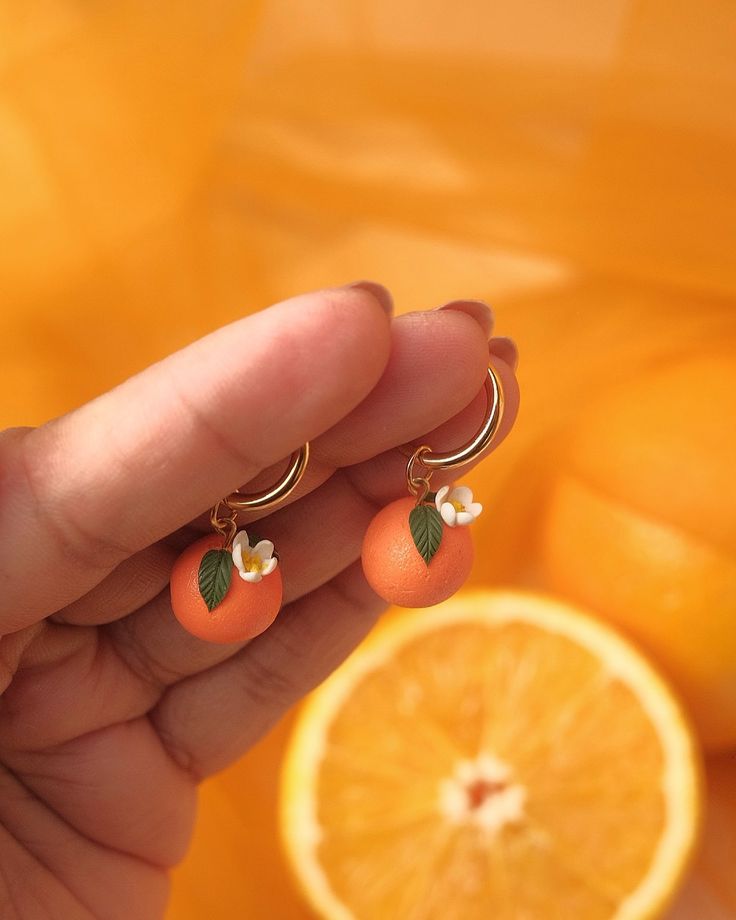 a person is holding an orange with two small leaves on it's earring