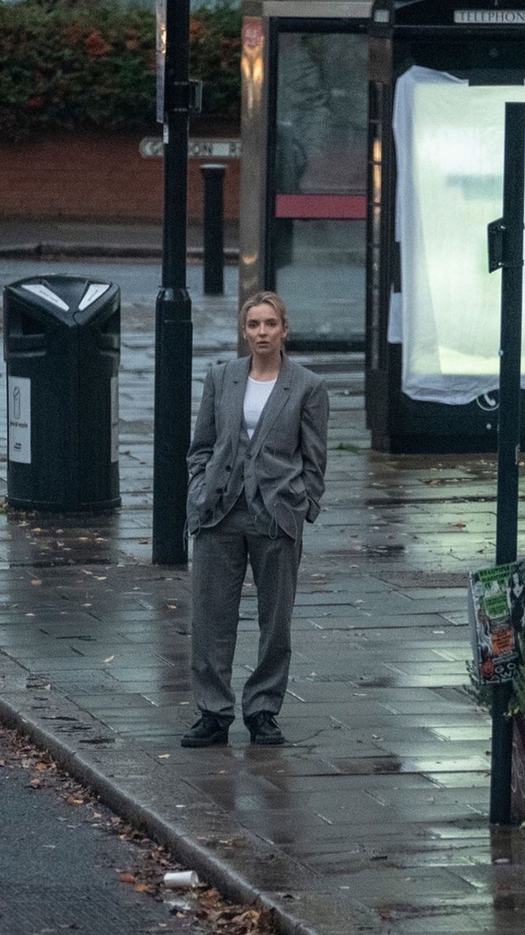 a woman is standing on the sidewalk in the rain