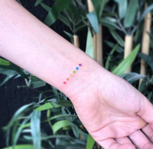 a person's arm with a small colorful dot tattoo on the left side of their arm