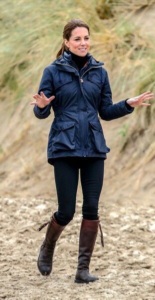 a woman in black jacket and brown boots walking on dirt ground with her hands out