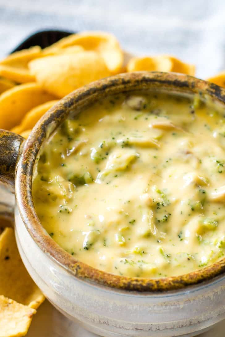 a white bowl filled with broccoli cheese dip surrounded by tortilla chips