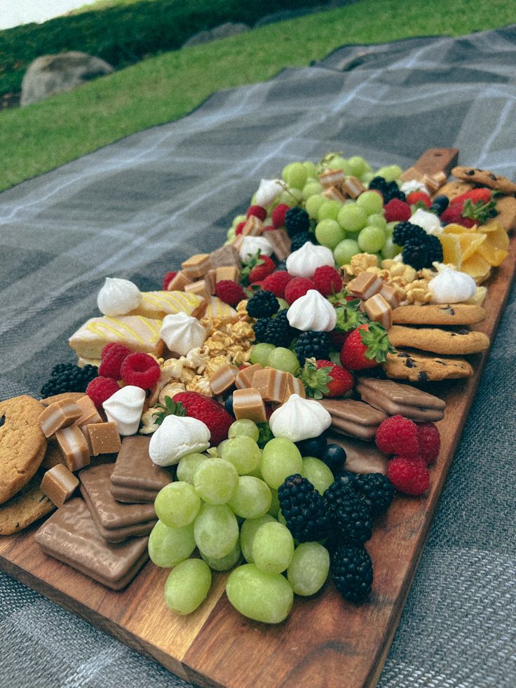 a wooden platter filled with grapes, cheese and crackers on top of a blanket