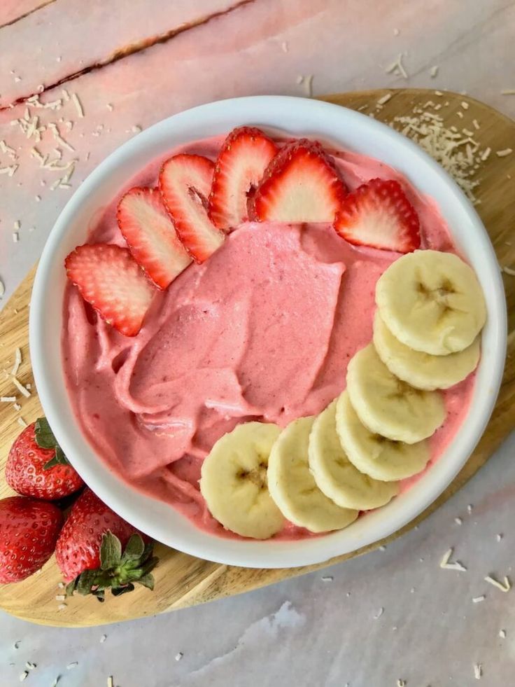 a bowl filled with fruit on top of a cutting board next to sliced bananas and strawberries