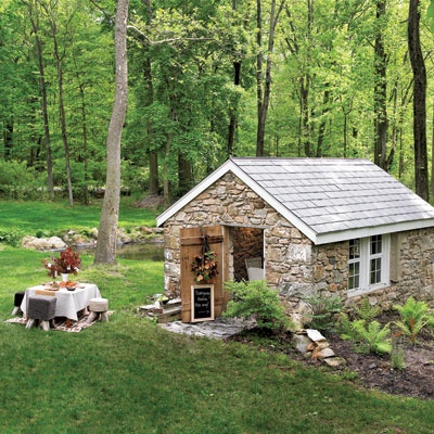 a small stone house in the middle of a forest with picnic table set up outside