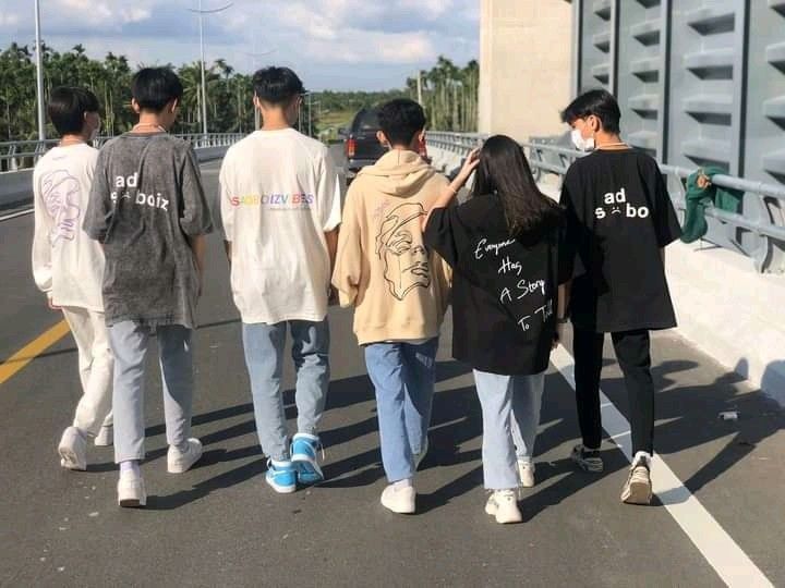 four people walking down the street wearing t - shirts with writing on them, and one person holding his hand out