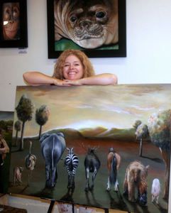 a woman is holding up a painting with animals on it in front of other paintings