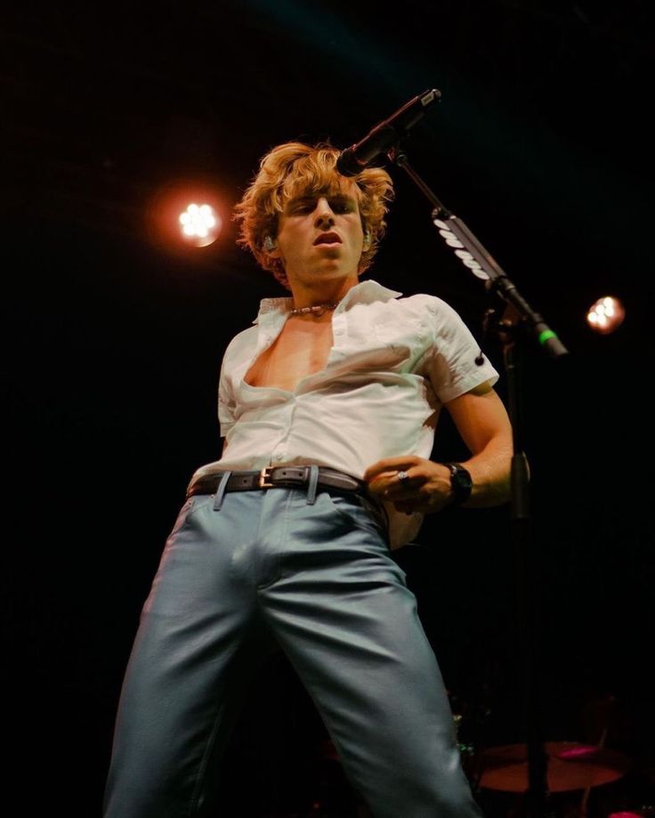 a man standing on top of a stage holding a microphone in his right hand and wearing blue pants