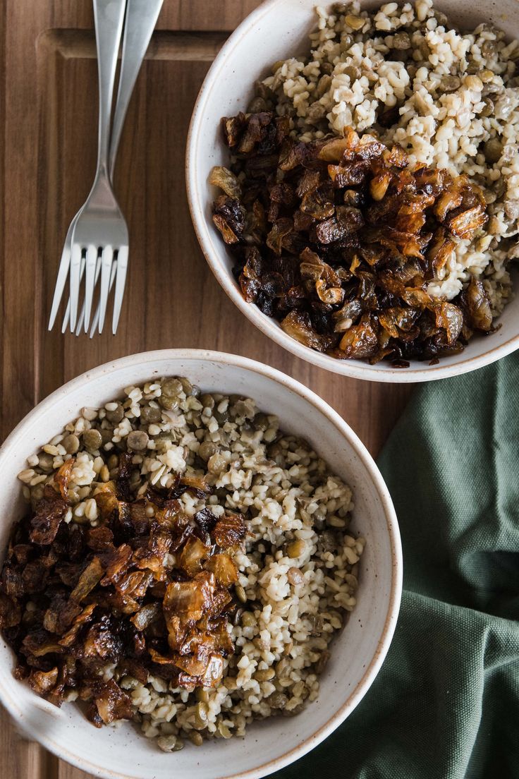 two white bowls filled with rice and meat next to a fork on top of a wooden table