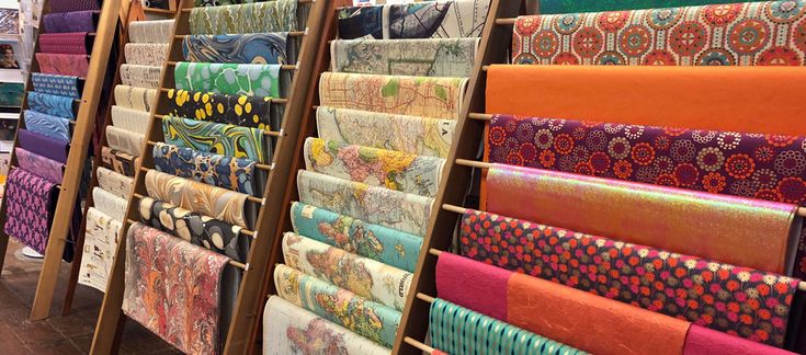 many different colored fabrics are on display in a store with wooden racks holding them up against the wall