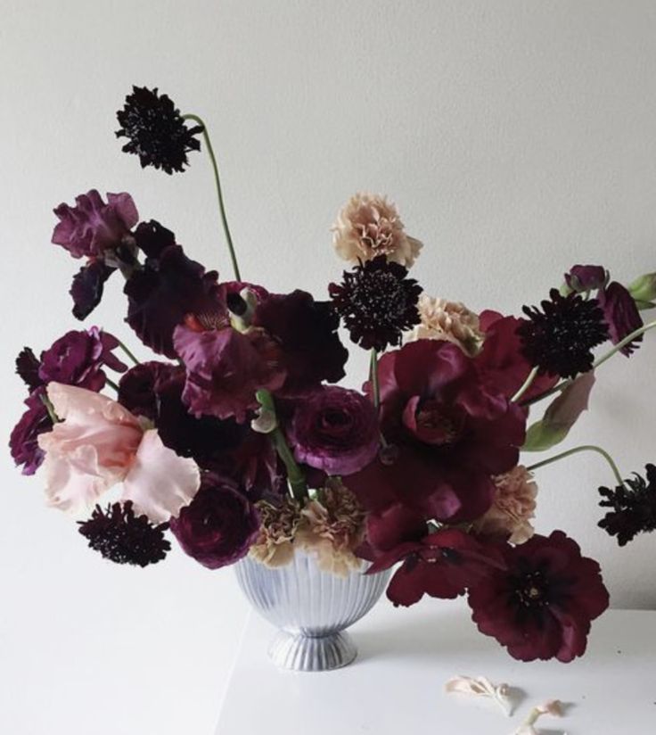 a vase filled with purple and pink flowers on top of a white table next to a wall