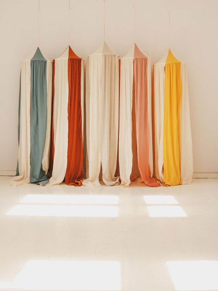 the curtains are lined up against the wall in different colors and sizes, along with sunlight coming through them