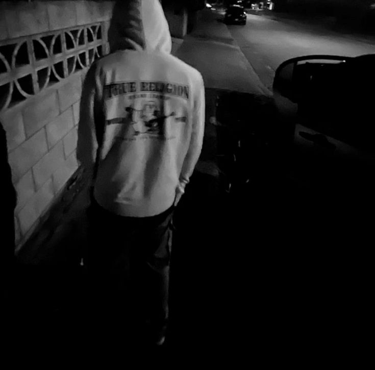 a man standing in front of a brick wall at night with his back to the camera