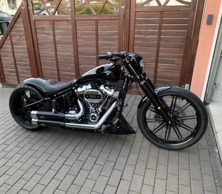 a black motorcycle parked in front of a garage door on brick road next to wooden fence