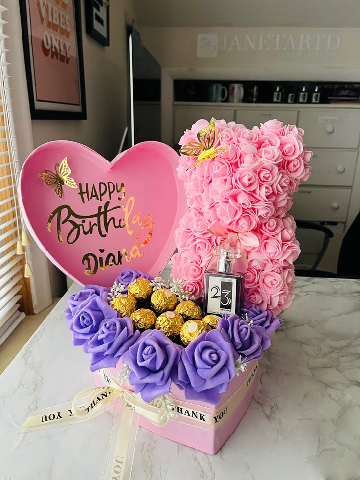 a pink heart shaped box filled with flowers and chocolates next to a bouquet of roses