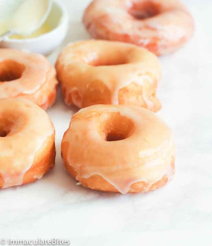 six glazed donuts sitting on top of a counter next to a bowl of butter